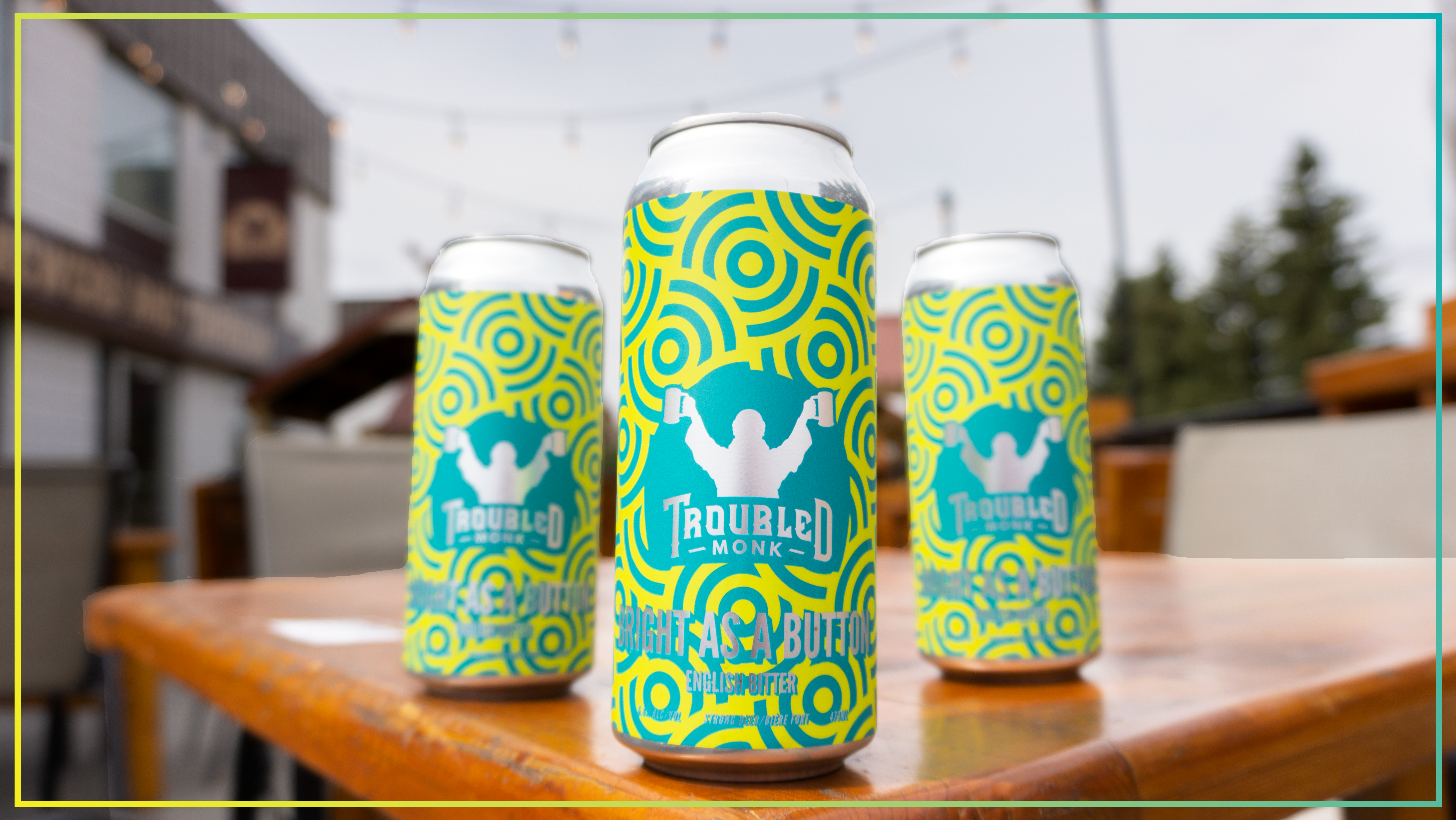 three cans of troubled monk bright as a button english bitter sitting on a wood patio table outside of the taproom.