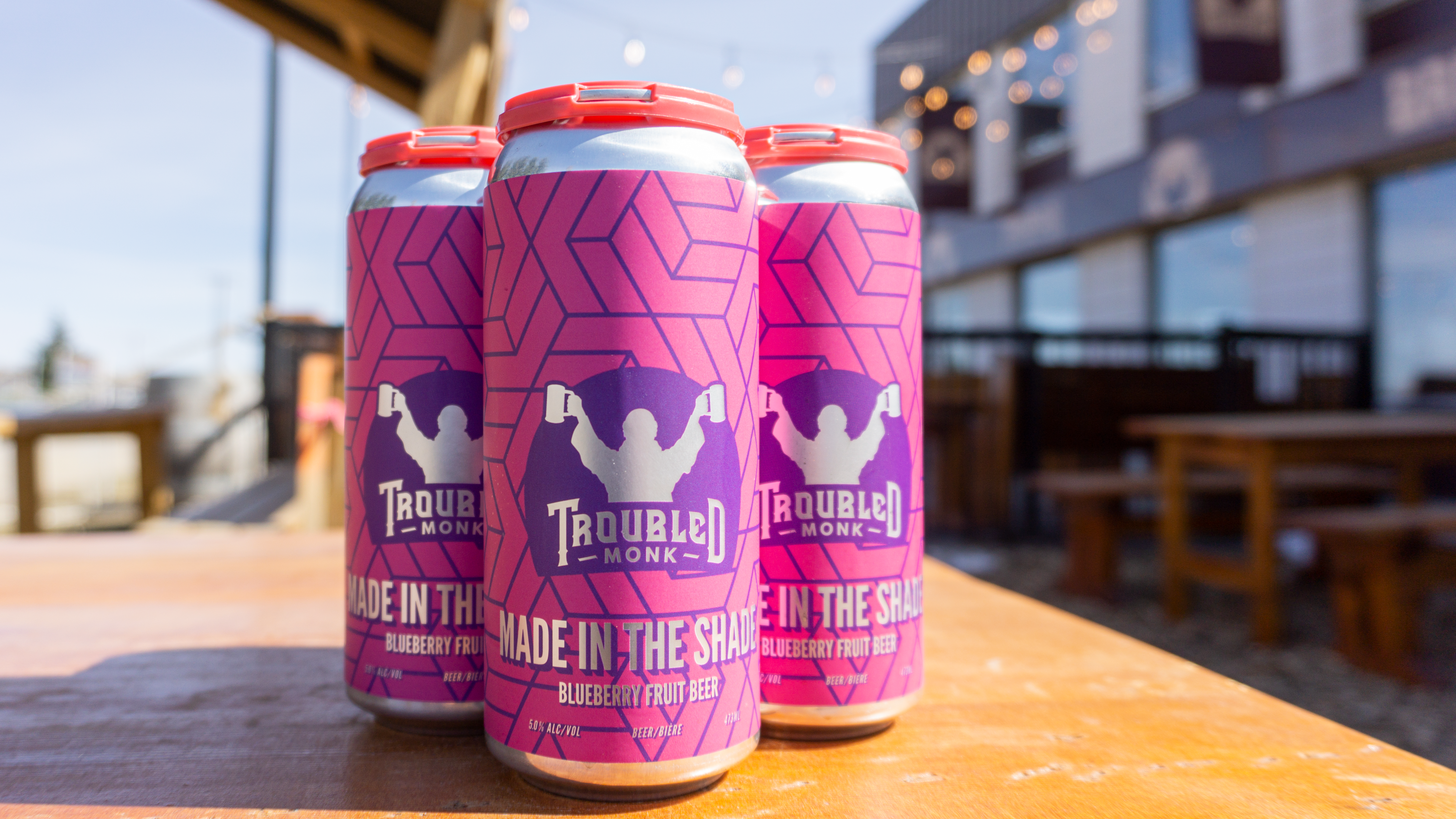 A four pack of tall cans of made in the shade blueberry fruit ale sitting on a table at troubled monk's patio.