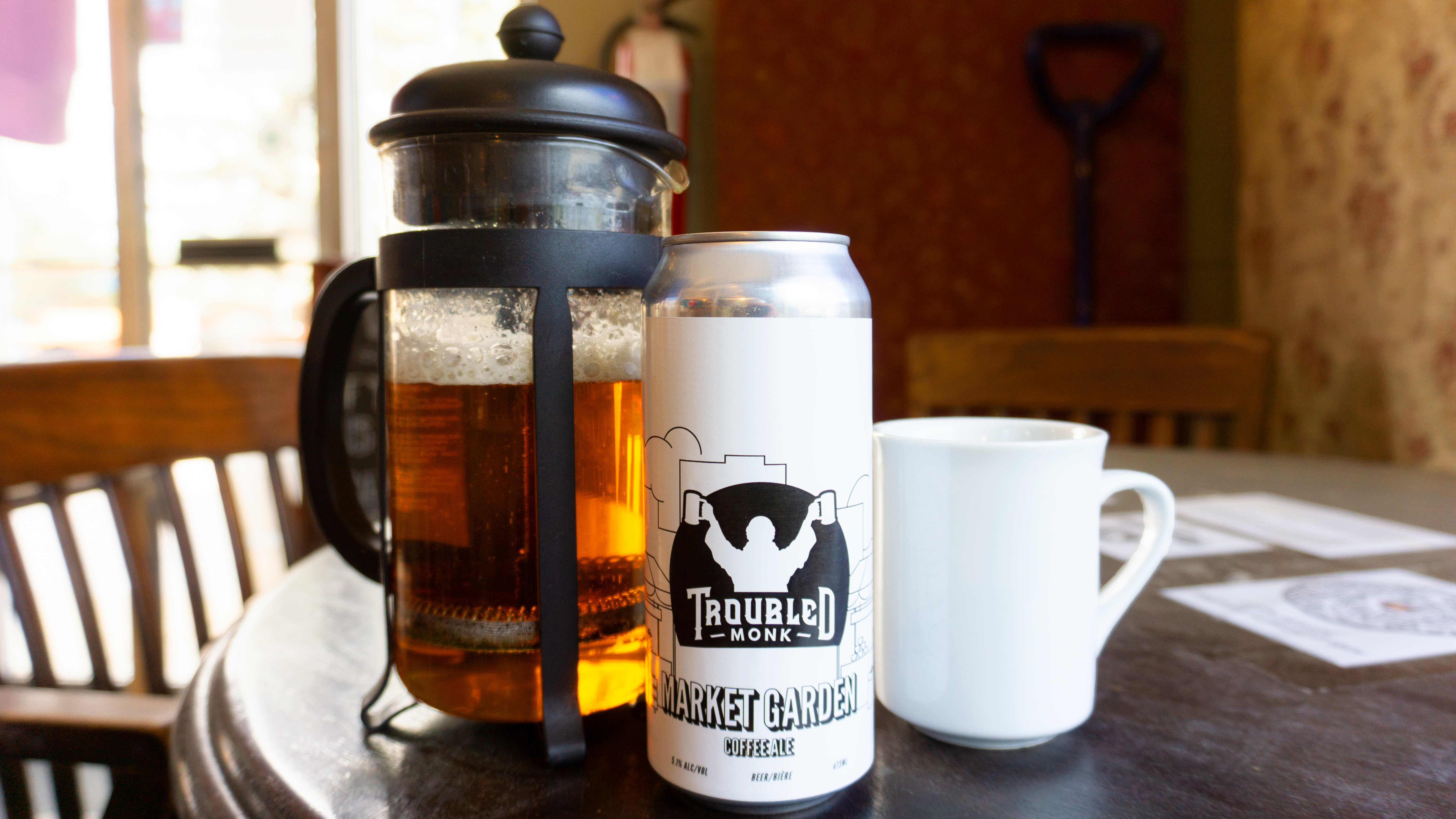 Picture of a coffee cup, a french press and a can of troubled monk's market garden coffee ale